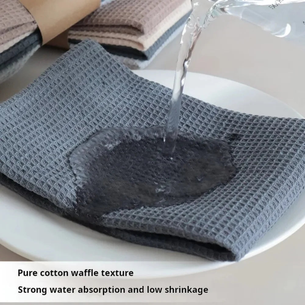 A gray cotton waffle weave towel is being filled with water on a white plate, demonstrating strong water absorption.