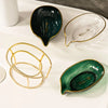 A set of decorative leaf soap dishes in green and clear glass with gold accents on a white tray.
