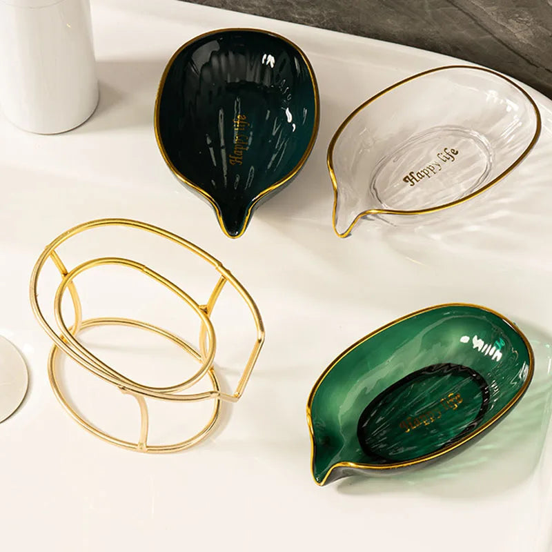 A set of decorative leaf soap dishes in green and clear glass with gold accents on a white tray.