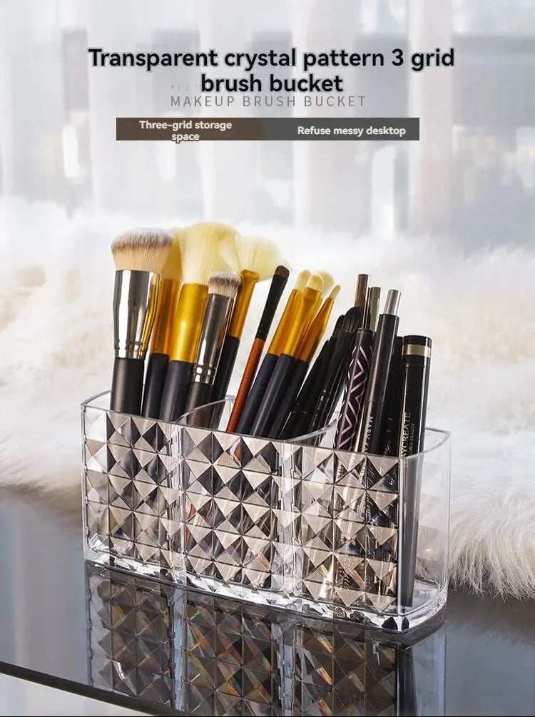 Clear acrylic makeup brush holder with three compartments displaying various makeup brushes.