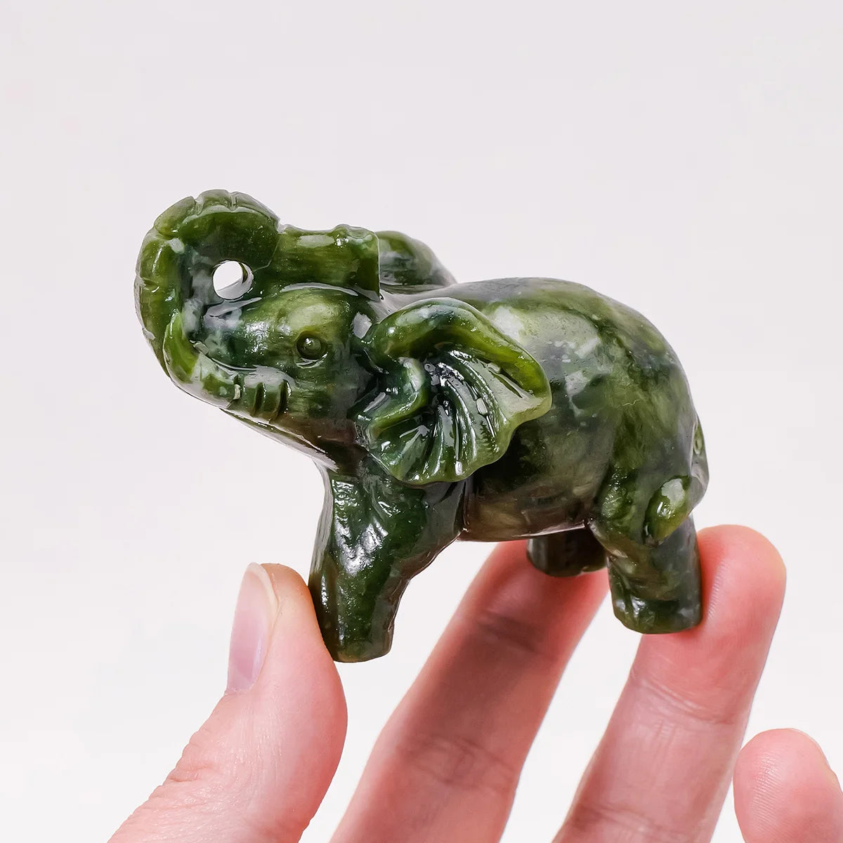 Hand-carved green jade elephant statue being held in a person's hand.