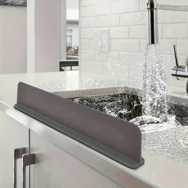 A gray silicone sink splash cover is installed over a kitchen sink, with water flowing from a faucet.