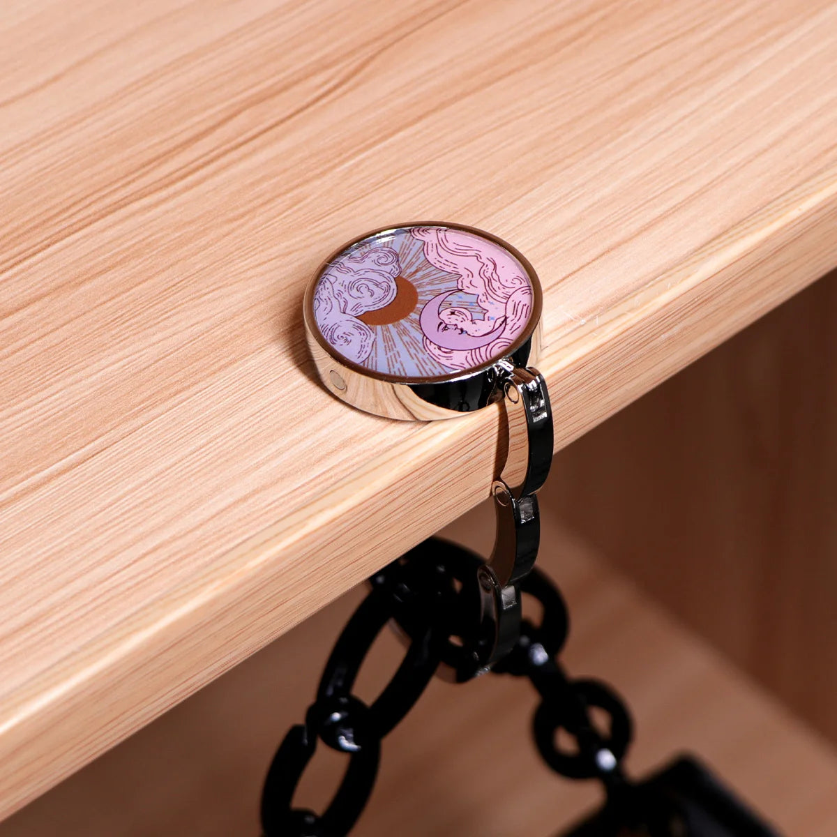 Silberner faltbarer Haken mit lila-goldenem Design auf hellem Holz