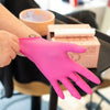Una mano con un guante desechable rosa brillante sostiene una caja de productos cosméticos.