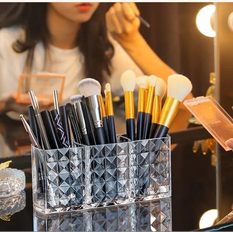 Clear acrylic makeup brush holder with three compartments filled with various makeup brushes