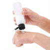 A hand is holding a white refillable travel bottle with a black cap.
