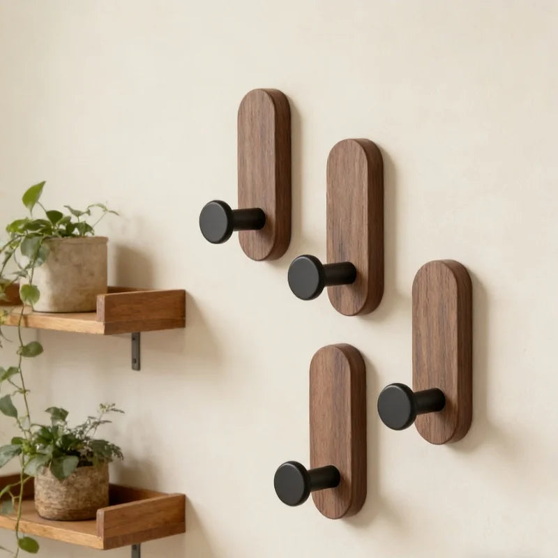 A set of three dark brown walnut wood wall hooks with self-adhesive mounting displayed against a light beige wall.