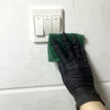 A hand wearing a black disposable nitrile cleaning glove is positioned next to a white electrical outlet with three switches.