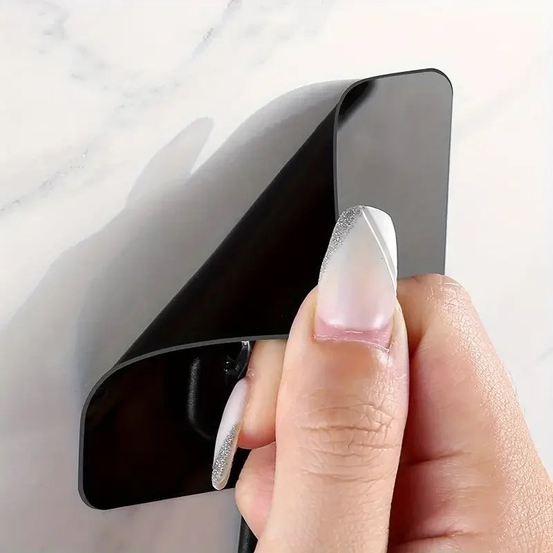 A hand holds a black heavy-duty self-adhesive wall hook against a white marble background.