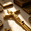 Primer plano de una cruz de metal dorado, posiblemente usada como pluma o decoración religiosa, sobre una superficie con otro