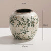 A white ceramic bud vase with green floral patterns and a dark rim, shown against a light background.