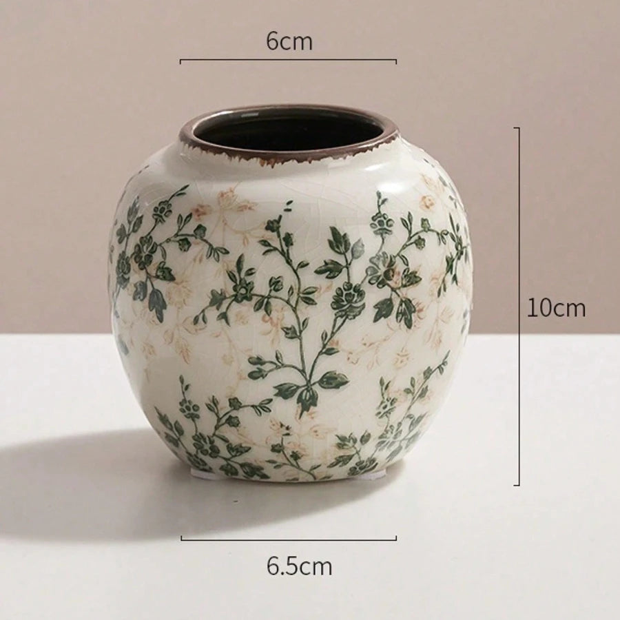 A white ceramic bud vase with green floral patterns and a dark rim, shown against a light background.