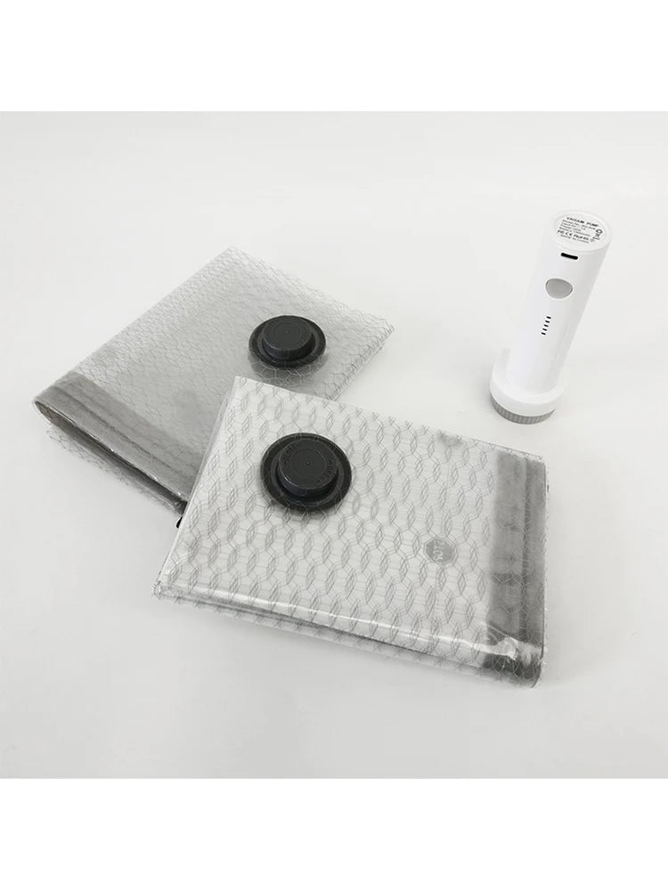 A clear vacuum compression travel bag and a white handheld vacuum device are shown on a white background.