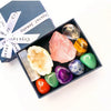A dark box holds a set of natural crystal stones including pink rose quartz, yellow citrine, and green jade.