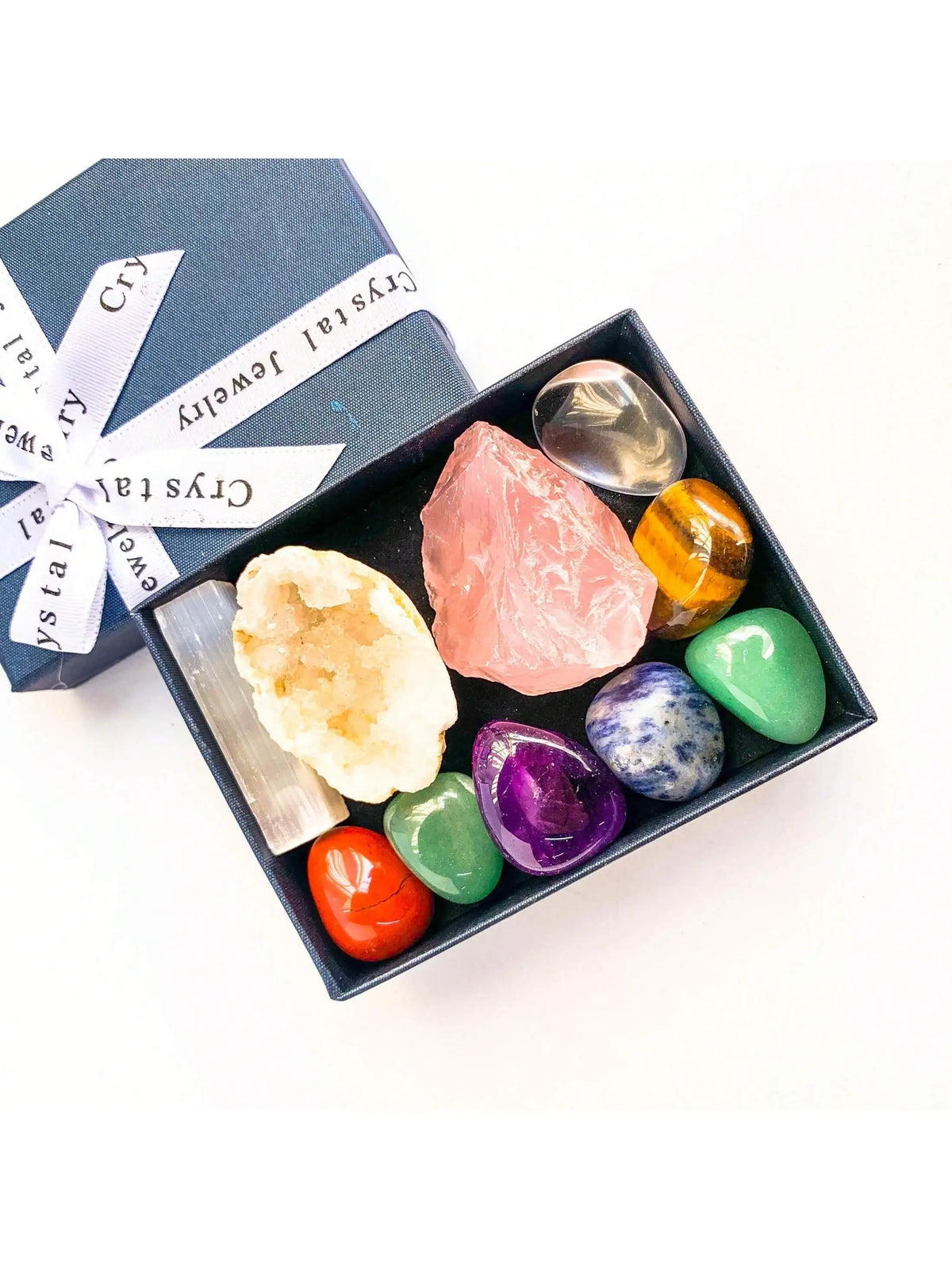A dark box holds a set of natural crystal stones including pink rose quartz, yellow citrine, and green jade.