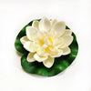 A white artificial lotus flower with yellow center resting on a green leaf.