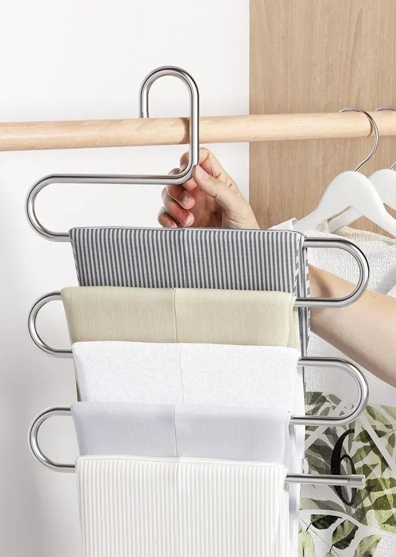 A multi-layer stainless steel clothes rack holding various folded white and beige fabric items.