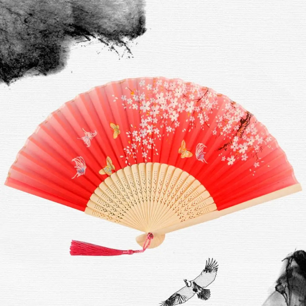 مروحة يدوية حمراء قابلة للطي بتصاميم زهور وردية وصفراء رقيقة على خلفية بيضاء.