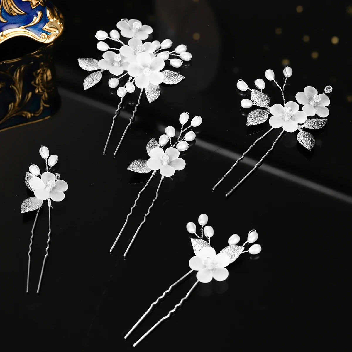 A set of white pearl flower bridal hair clips with silver accents displayed on a dark surface.