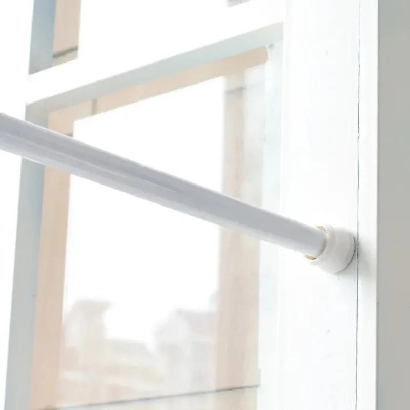 A white adjustable telescopic curtain rod extending horizontally across a window frame.