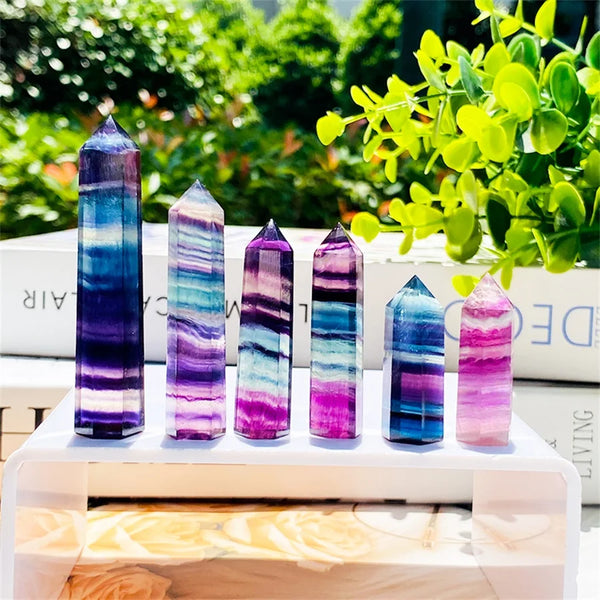 A display of nine natural fluorite healing crystal wands in various shades of purple and blue on a white surface.