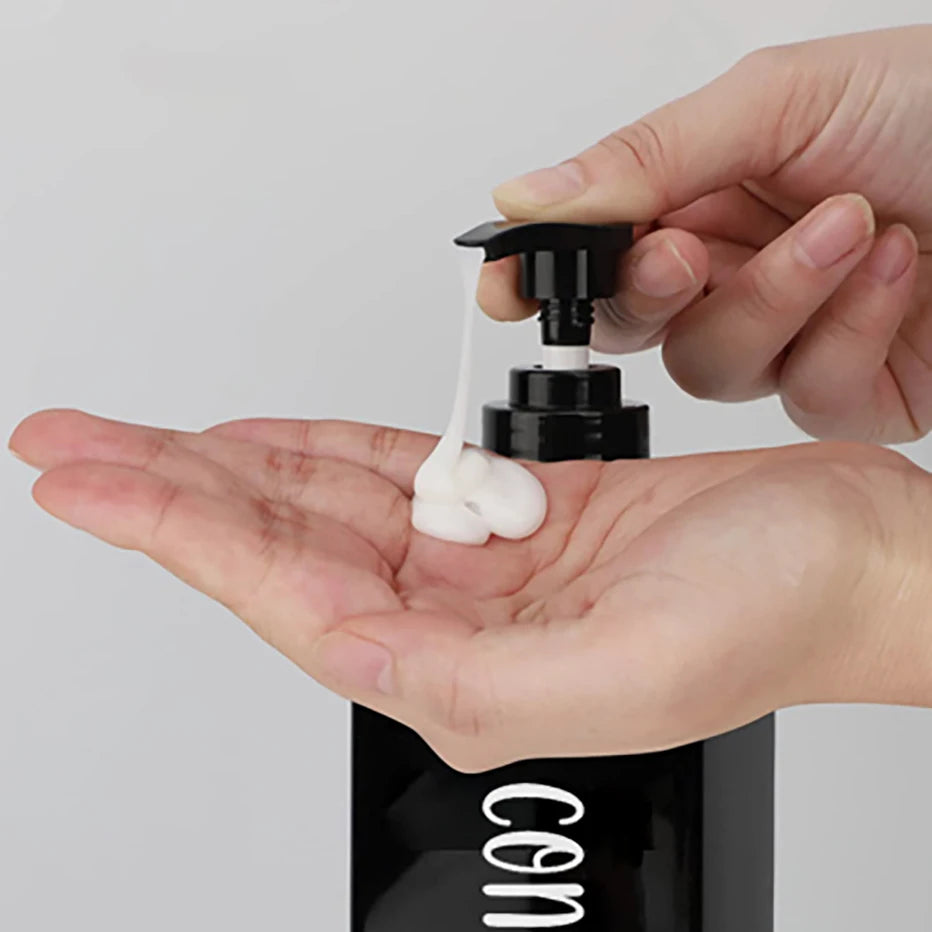 A hand is squeezing white body wash from a black pump bottle onto an open palm.
