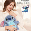A young woman is holding a blue cartoon plush toy, which is a hot water bottle, in a cozy indoor setting.