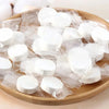 A pile of white disposable compressed travel towels packaged in clear plastic on a wooden board.