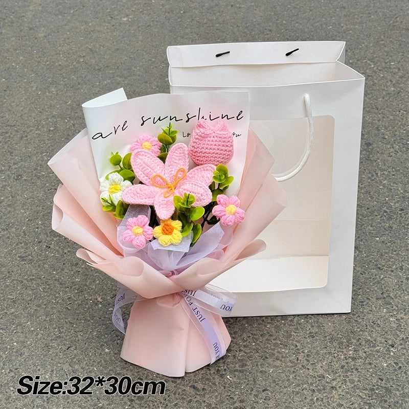 A bouquet of pink and yellow handmade crochet flowers wrapped in sheer paper placed inside a white paper shopping bag.