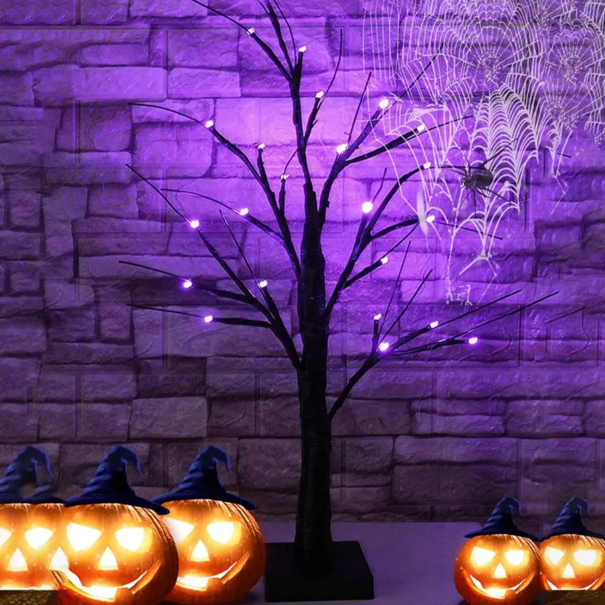 Dunkle Baumsilhouette, beleuchtet von lila Lichterketten vor einer Steinmauer mit leuchtenden orangen Jack-o'-Lanterns.