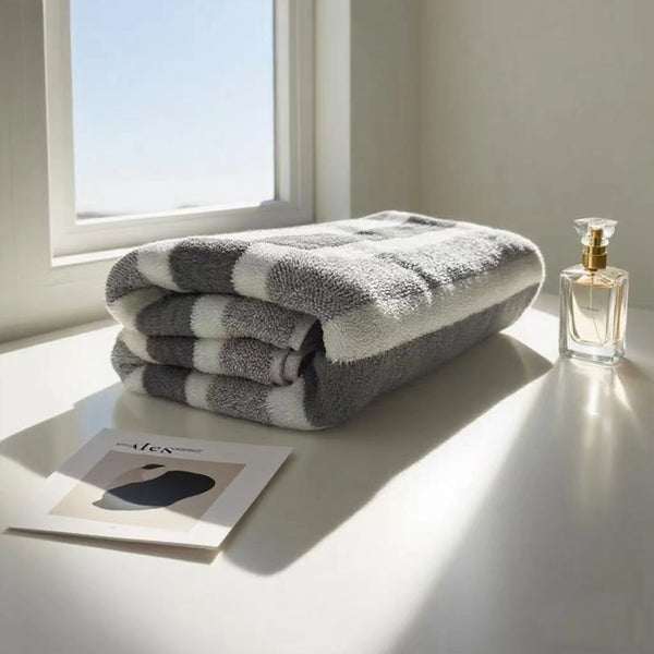 A stack of gray and white striped quick-dry bath towels next to a glass perfume bottle on a white windowsill.