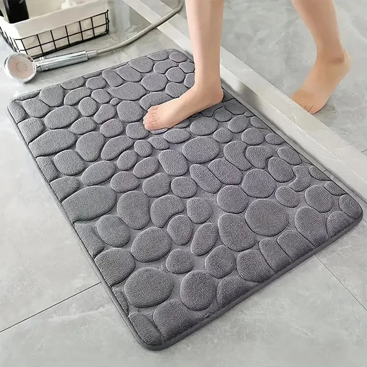 A gray, textured 3D non-slip bathroom doormat placed on a light tile floor.
