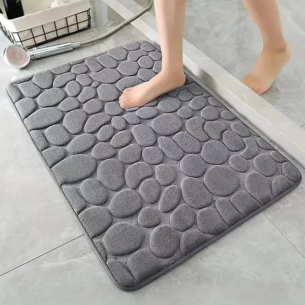 A gray, textured 3D non-slip bathroom doormat placed on a light tile floor.