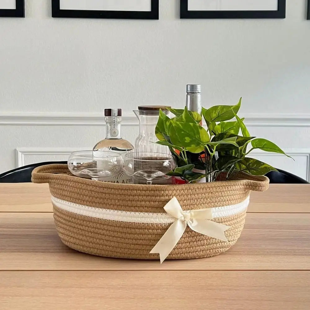 A woven cotton rope storage basket filled with glass bottles and a green plant on a wooden table.