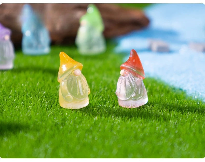 Three luminous resin mini fairy gnomes in yellow, green, and orange standing on bright green grass.
