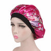 A satin sleep bonnet in pink with floral embroidery worn on a mannequin head.