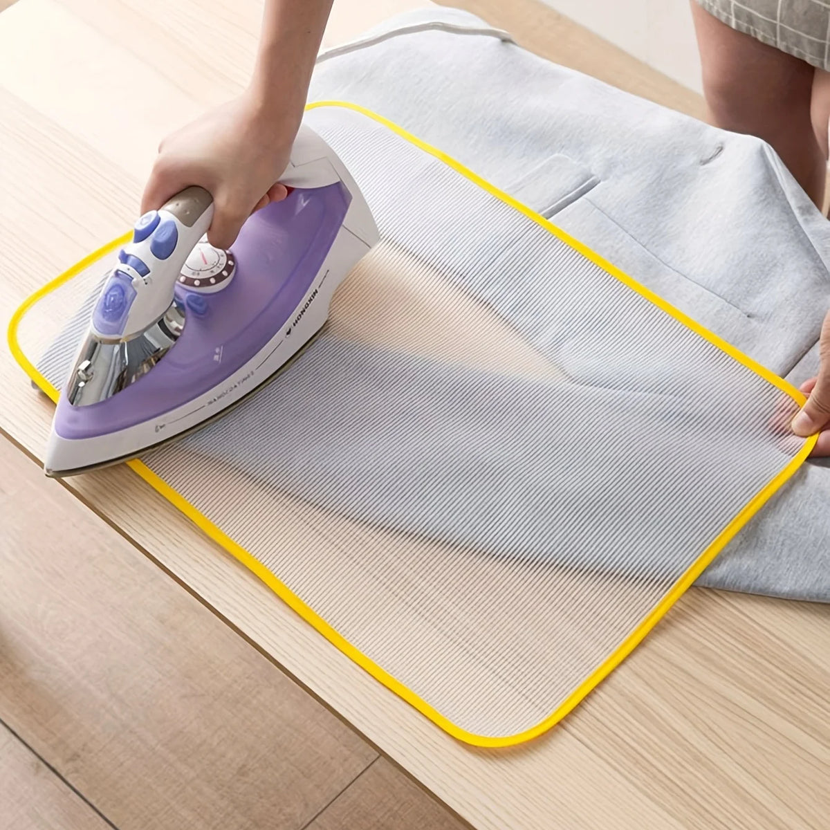 A purple heat resistant ironing cloth is being used with a steam iron on a light wooden table.