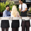 Eine Person trägt eine schwarze Server-Schürze mit praktischen Taschen, von der Taille abwärts sichtbar.