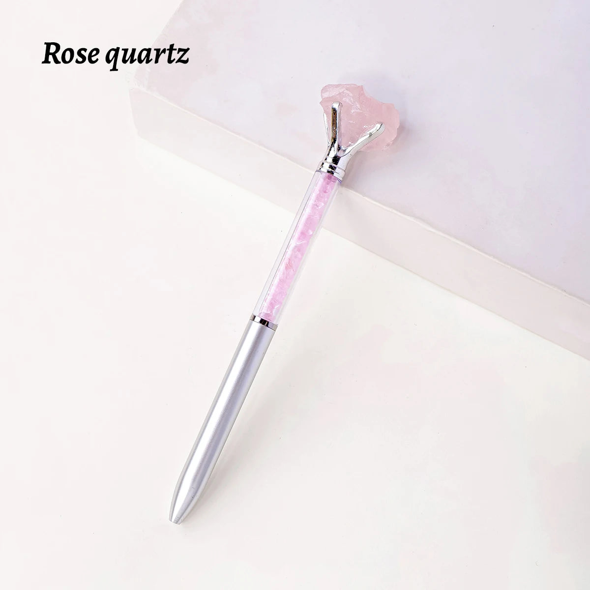 A silver crystal pen with a pink rose quartz gemstone is displayed on a white surface.