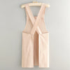 A light beige cotton kitchen apron with criss-cross straps hanging on a wooden hanger.