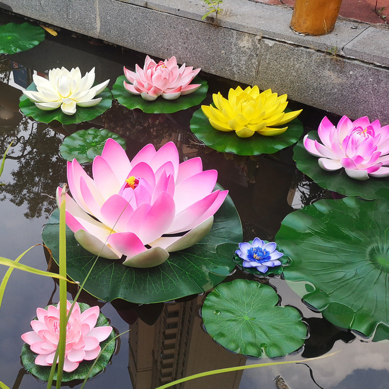 A collection of artificial pink, white, and yellow lotus flowers floating on green lily pads in water.