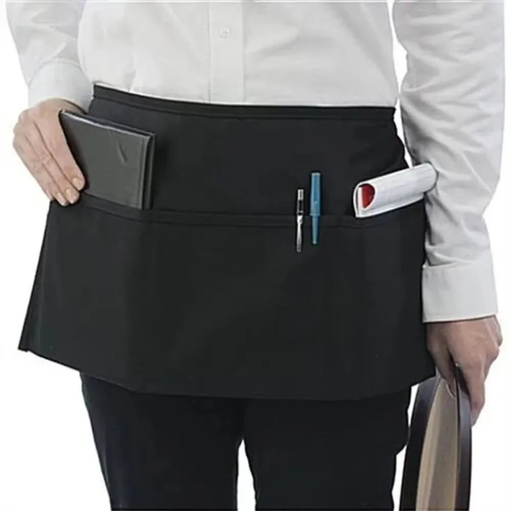 A black fashion chef short apron with pockets worn by a person in a white shirt.