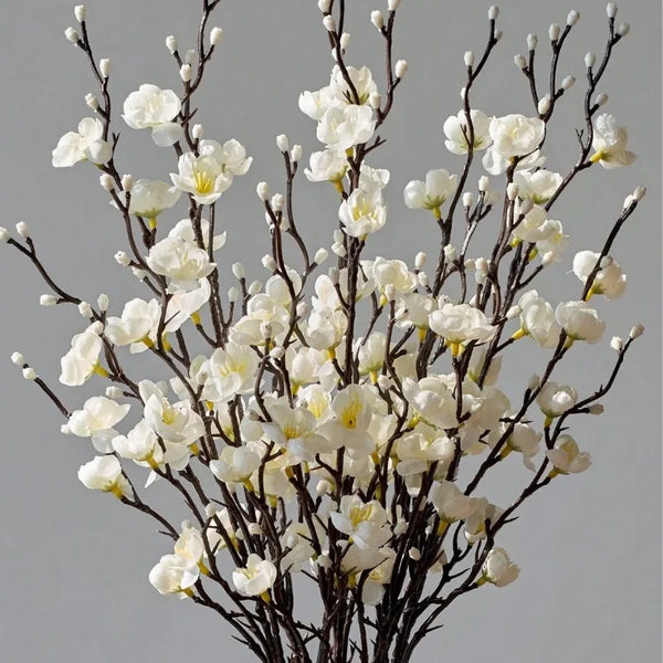 A branch of artificial white plum blossoms with delicate flowers and dark branches.