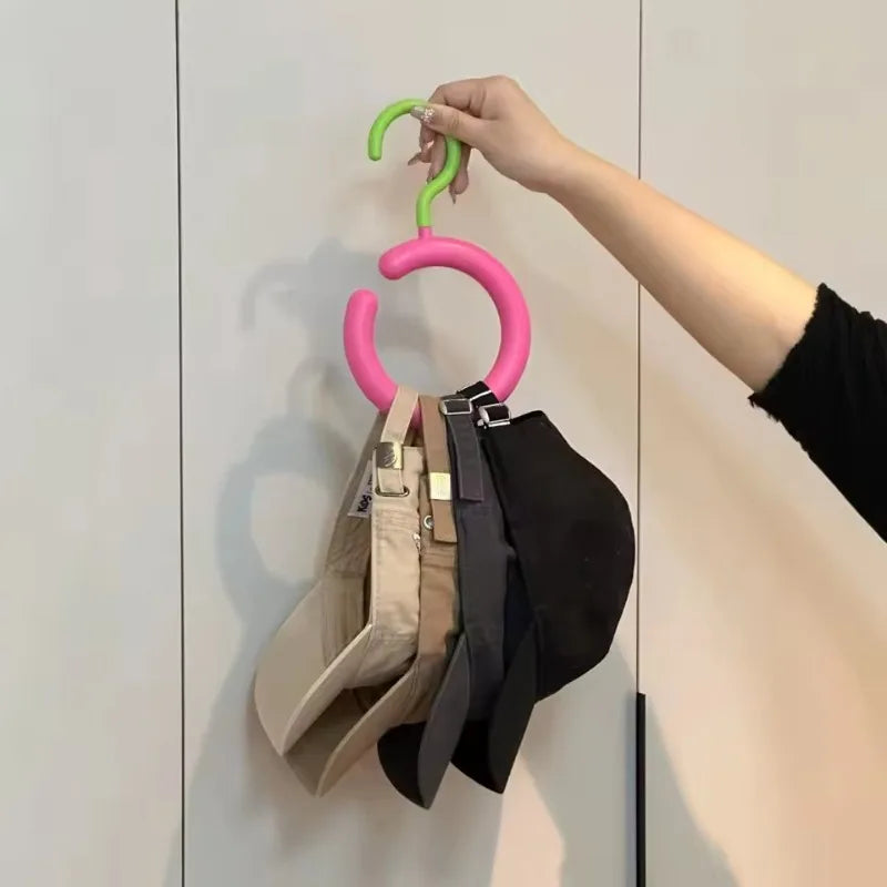 Une main accroche un cintre invisible multifonction avec des crochets verts et roses sur un mur blanc.