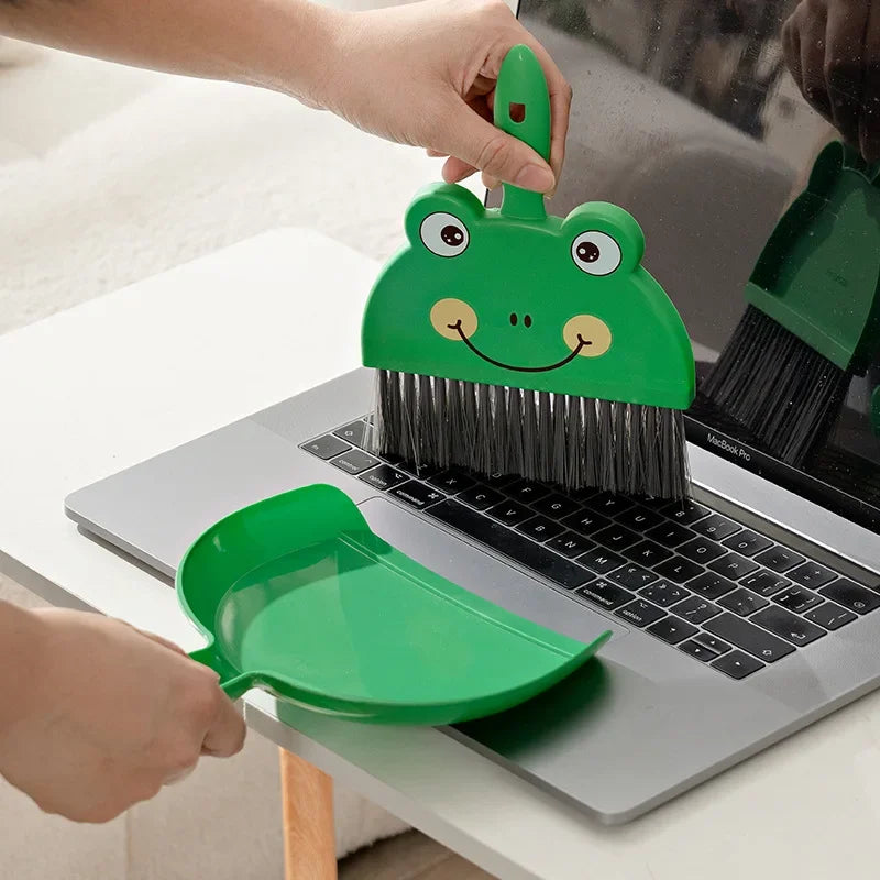 A hand is using a green cartoon animal broom and dustpan set on a laptop.
