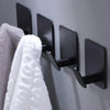 Black stainless steel adhesive hooks mounted on a gray wall, used for hanging towels or kitchen items.