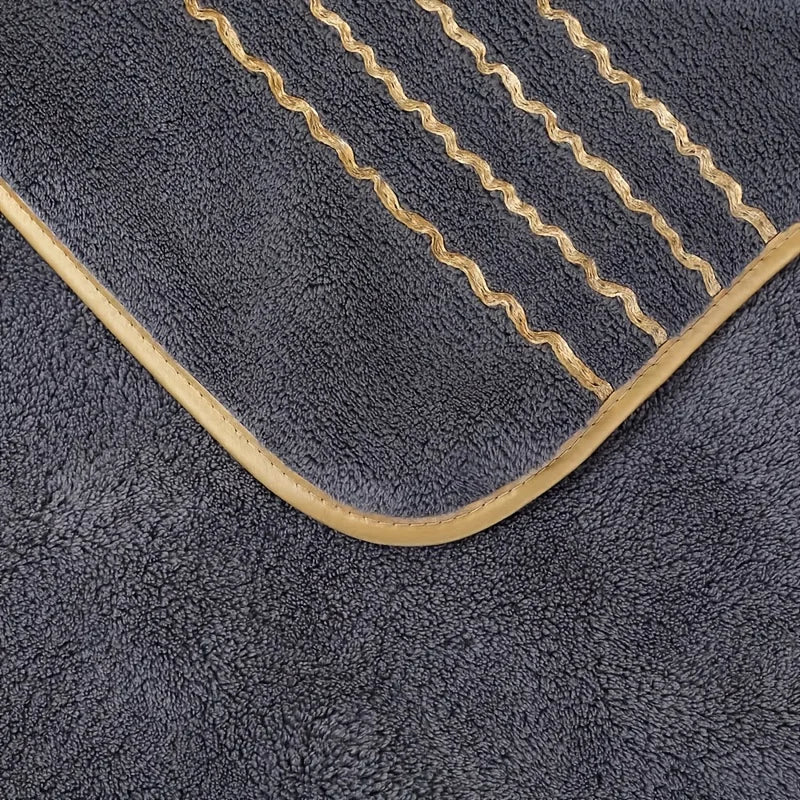 A dark gray coral fleece towel featuring gold stripe detailing and a curved edge.