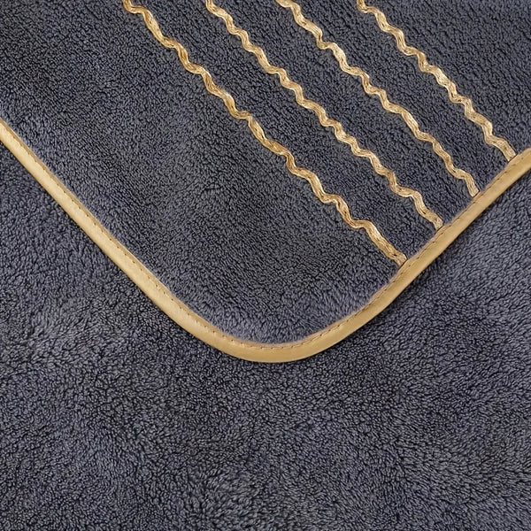 A dark gray coral fleece towel featuring gold stripe detailing and a curved edge.