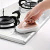 A hand is using a pink magic sponge scrubber with an ergonomic handle to clean a stovetop.
