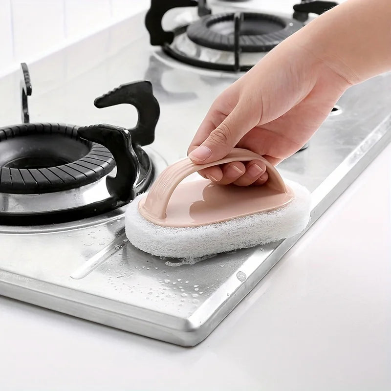 A hand is using a pink magic sponge scrubber with an ergonomic handle to clean a stovetop.